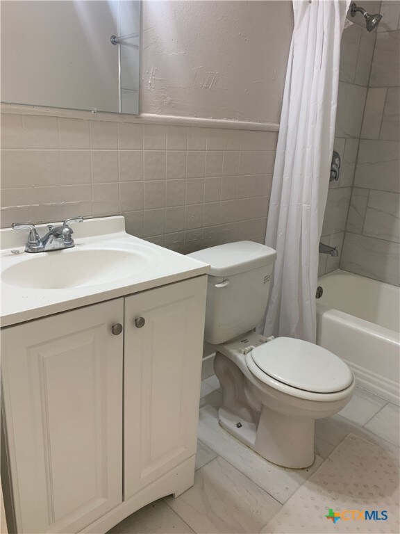 full bathroom featuring vanity, shower / bathtub combination with curtain, tile walls, and toilet