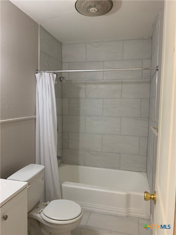 full bathroom featuring shower / bath combo with shower curtain, vanity, toilet, and tile walls