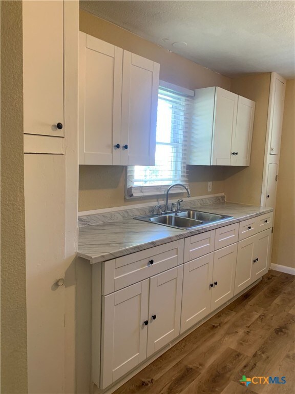 kitchen featuring white cabinetry, sink, light wood-type flooring, and a textured ceiling