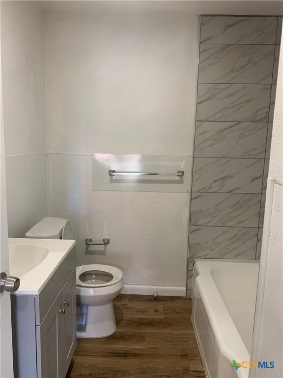 bathroom featuring hardwood / wood-style flooring, vanity, a washtub, toilet, and tile walls