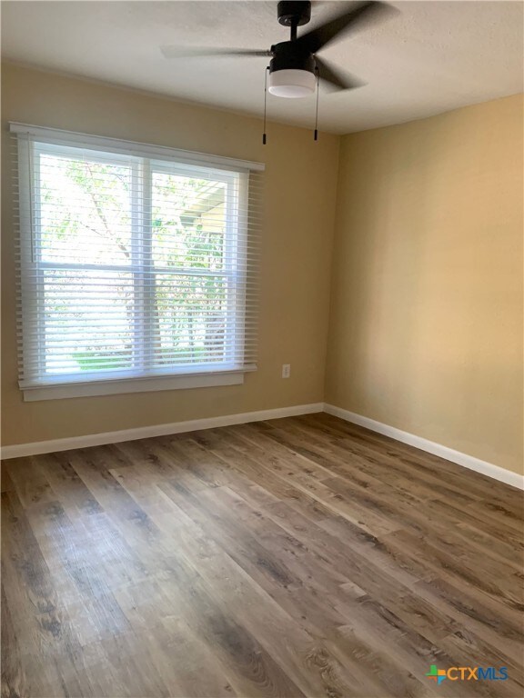 empty room with dark wood-type flooring, a healthy amount of sunlight, and ceiling fan