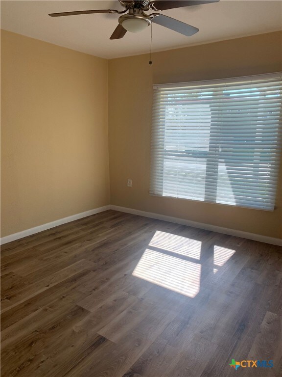 empty room with dark wood-type flooring and ceiling fan