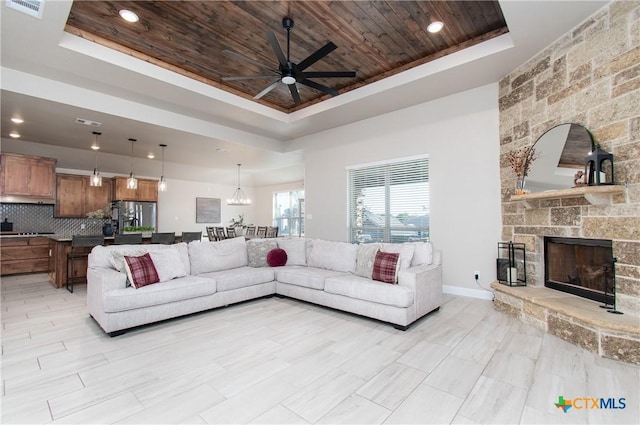 living room featuring a tray ceiling, a stone fireplace, ceiling fan, and wood ceiling