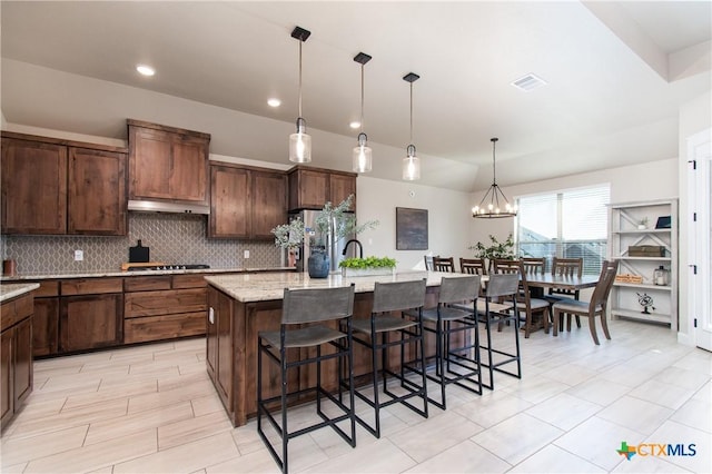 kitchen with stainless steel refrigerator, light stone countertops, a kitchen breakfast bar, an island with sink, and decorative light fixtures