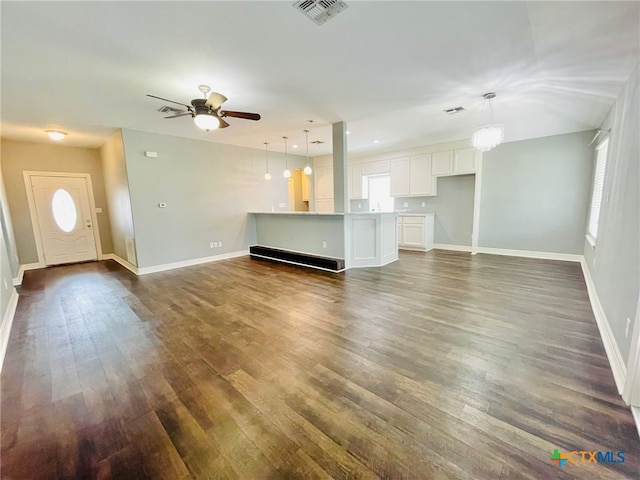 unfurnished living room with plenty of natural light, dark wood-type flooring, and ceiling fan with notable chandelier