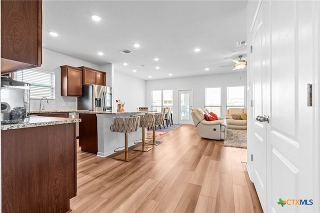 kitchen featuring a kitchen bar, light wood-style floors, stainless steel fridge, a ceiling fan, and a sink