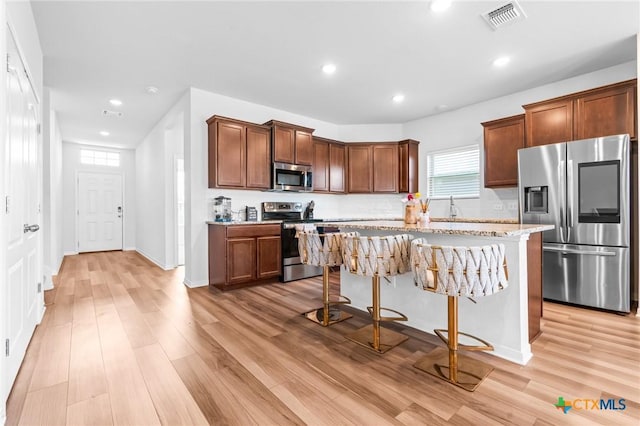 kitchen featuring visible vents, a kitchen island, light wood-type flooring, a kitchen breakfast bar, and stainless steel appliances