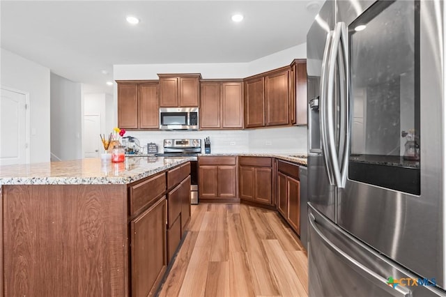 kitchen featuring backsplash, a center island, light stone counters, light wood-style flooring, and stainless steel appliances