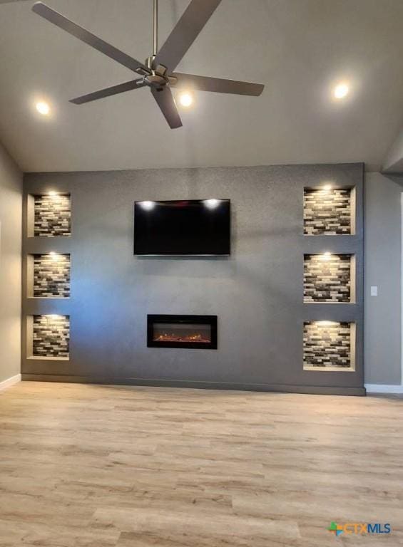 unfurnished living room featuring a glass covered fireplace, wood finished floors, a ceiling fan, and baseboards