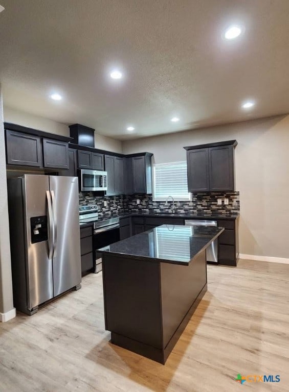 kitchen featuring a sink, a center island, baseboards, decorative backsplash, and appliances with stainless steel finishes
