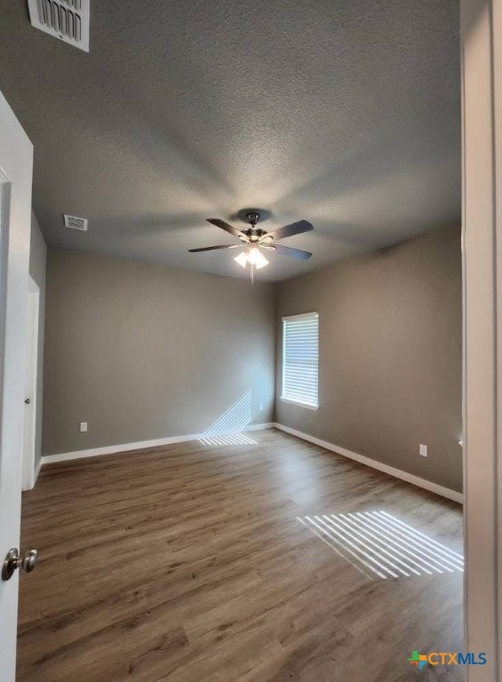 spare room featuring wood finished floors, visible vents, baseboards, and ceiling fan