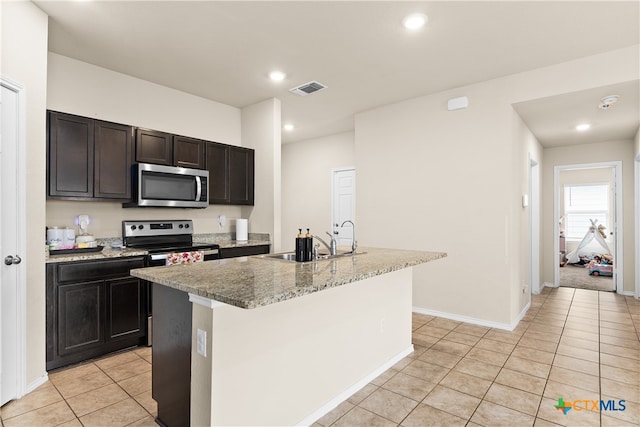 kitchen with stainless steel appliances, a center island with sink, sink, light stone countertops, and light tile patterned floors