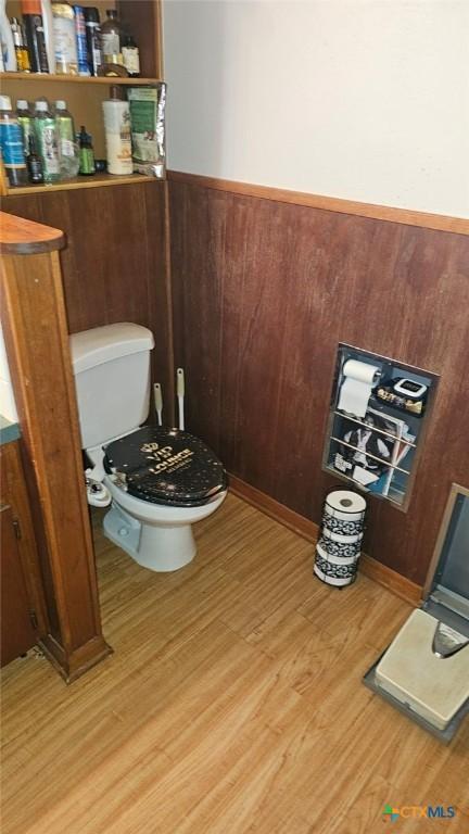 bathroom featuring wood-type flooring, wooden walls, and toilet