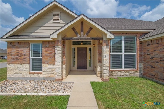 view of front of home featuring a shingled roof, a front yard, and stone siding