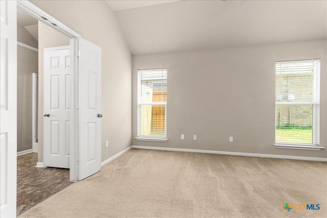 spare room featuring light carpet, lofted ceiling, and a wealth of natural light