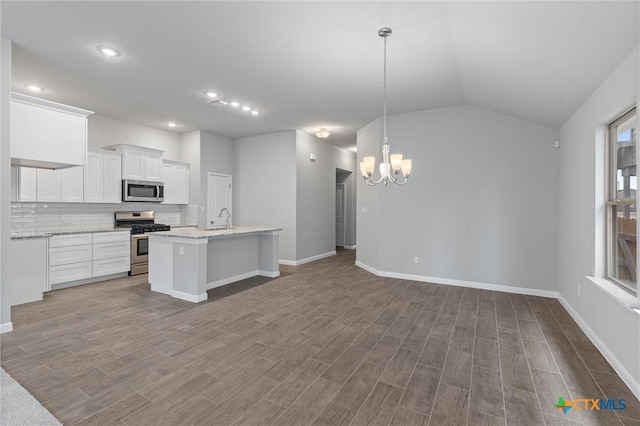 kitchen with appliances with stainless steel finishes, white cabinetry, decorative backsplash, hanging light fixtures, and a kitchen island with sink