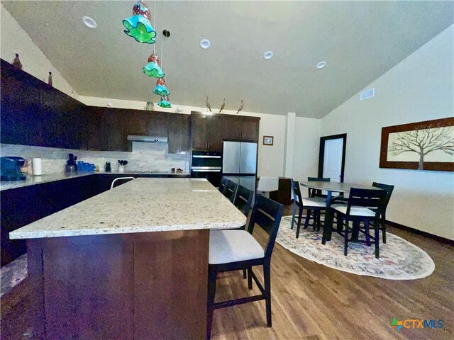 kitchen with tasteful backsplash, hardwood / wood-style floors, hanging light fixtures, a kitchen island, and stainless steel fridge