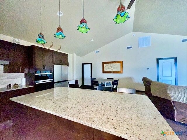 kitchen with white fridge, dark brown cabinets, light stone countertops, pendant lighting, and vaulted ceiling