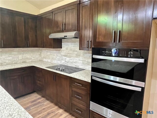 kitchen featuring black electric cooktop, dark brown cabinetry, light stone countertops, light hardwood / wood-style flooring, and double oven