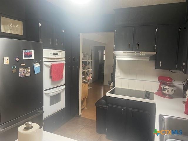 kitchen featuring light tile patterned flooring, stainless steel refrigerator, double oven, tasteful backsplash, and black electric cooktop