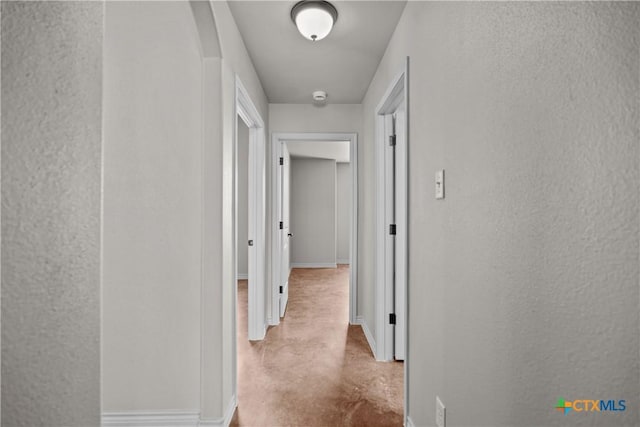 corridor with concrete flooring, a textured wall, and baseboards