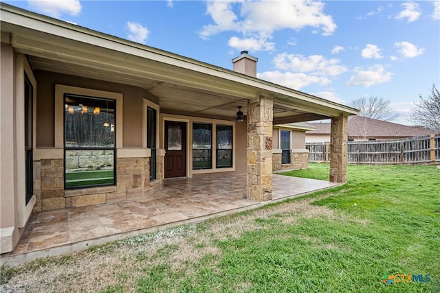 rear view of property featuring a patio, fence, a yard, stucco siding, and a chimney