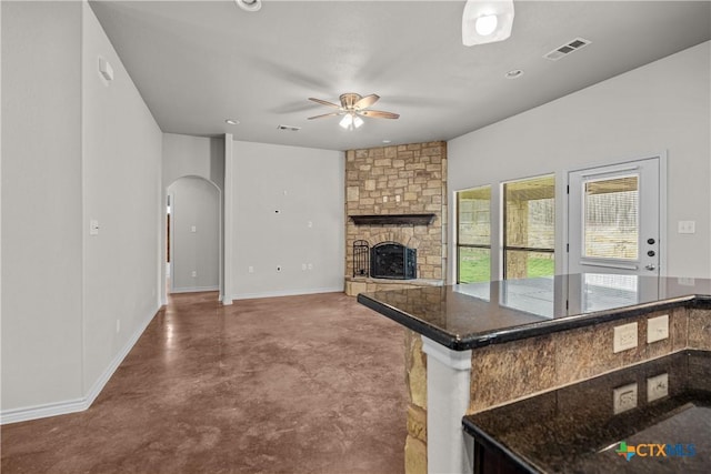 kitchen with arched walkways, a stone fireplace, a ceiling fan, visible vents, and finished concrete floors