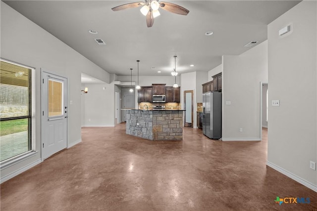 kitchen with ceiling fan, baseboards, appliances with stainless steel finishes, an island with sink, and finished concrete floors