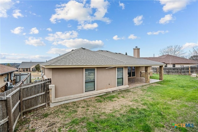 rear view of house with a fenced backyard, a shingled roof, a lawn, stucco siding, and a patio area