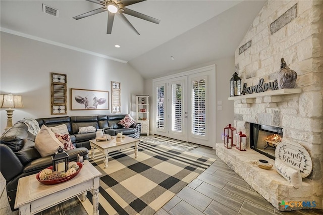 living room featuring a stone fireplace, french doors, vaulted ceiling, ceiling fan, and crown molding