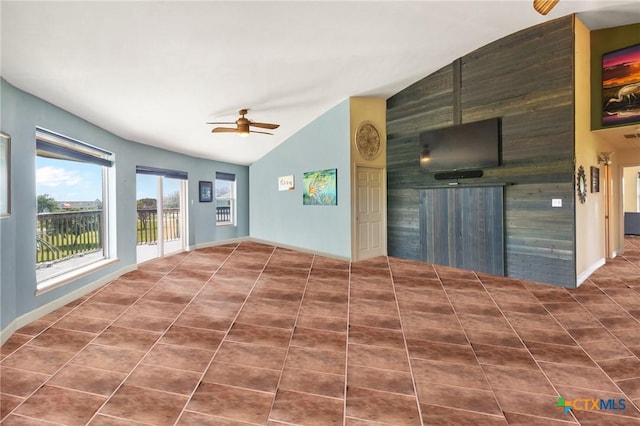 empty room with ceiling fan, vaulted ceiling, and dark tile patterned floors