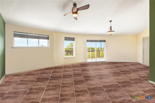 unfurnished room with a wealth of natural light, dark tile patterned flooring, and ceiling fan