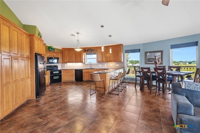 kitchen featuring sink, a breakfast bar area, a center island, hanging light fixtures, and black appliances