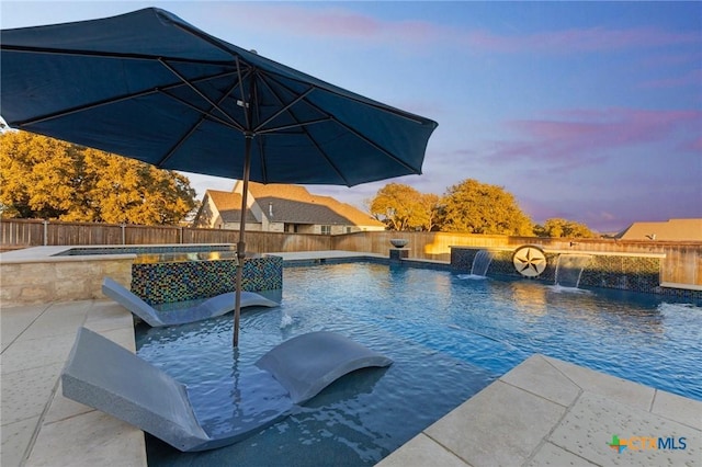 pool at dusk featuring pool water feature and an in ground hot tub