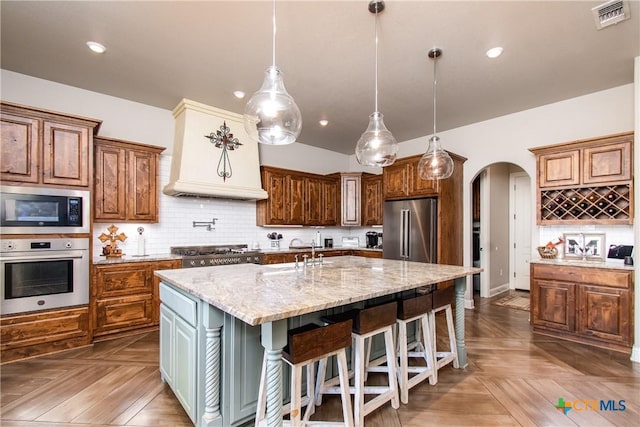 kitchen featuring dark parquet flooring, backsplash, a kitchen island with sink, hanging light fixtures, and stainless steel appliances