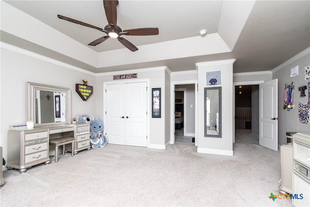 bedroom with light carpet, ornamental molding, a tray ceiling, ceiling fan, and a closet