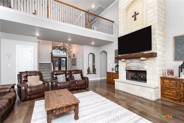 living room featuring a high ceiling, a stone fireplace, dark wood-type flooring, and a notable chandelier