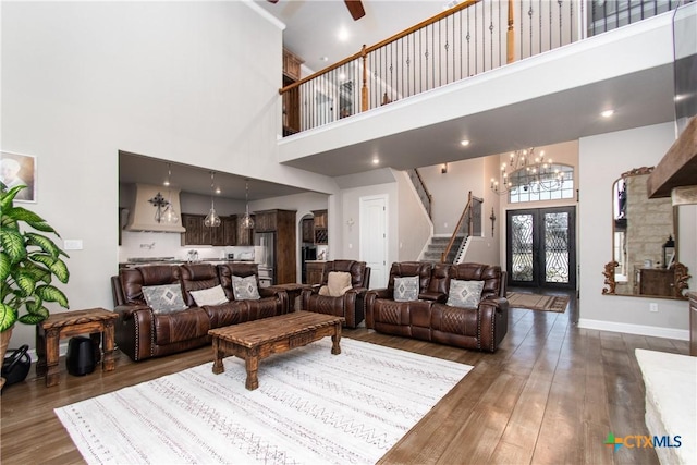 living room featuring french doors, a towering ceiling, dark wood-type flooring, and ceiling fan with notable chandelier