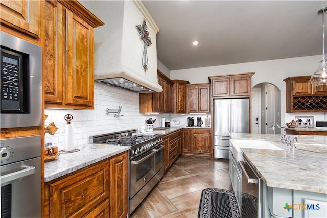 kitchen featuring backsplash, sink, hanging light fixtures, light stone counters, and stainless steel appliances