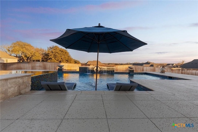 pool at dusk featuring pool water feature and a patio area