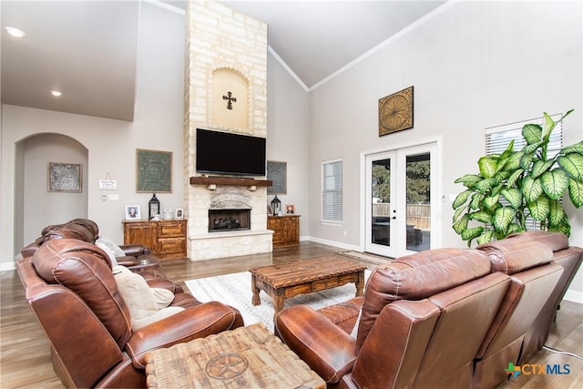 living room with high vaulted ceiling, french doors, a stone fireplace, light wood-type flooring, and ornamental molding