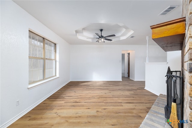 unfurnished living room with light hardwood / wood-style floors, a raised ceiling, and ceiling fan