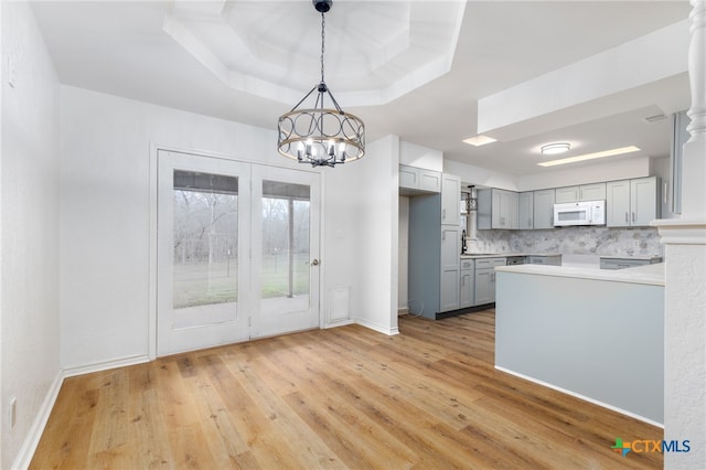 kitchen featuring tasteful backsplash, a tray ceiling, a notable chandelier, gray cabinets, and hanging light fixtures