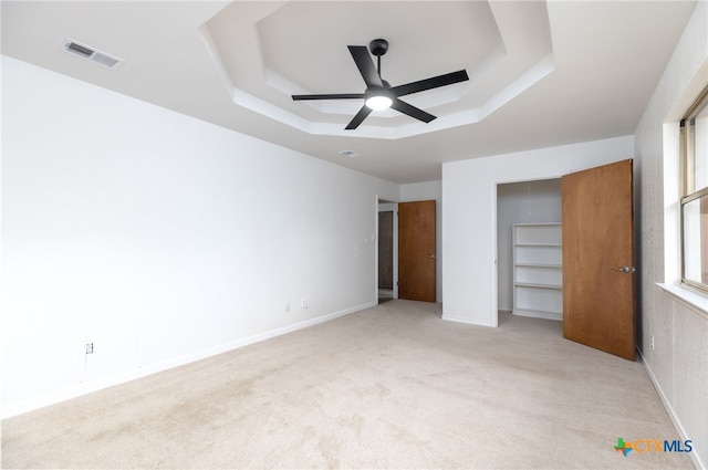 unfurnished bedroom featuring ceiling fan, a raised ceiling, light colored carpet, and a closet