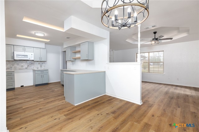 kitchen featuring hardwood / wood-style floors, ceiling fan with notable chandelier, decorative backsplash, gray cabinets, and kitchen peninsula