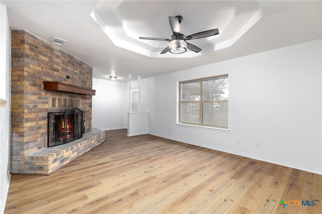 unfurnished living room featuring a tray ceiling, light hardwood / wood-style floors, and a brick fireplace