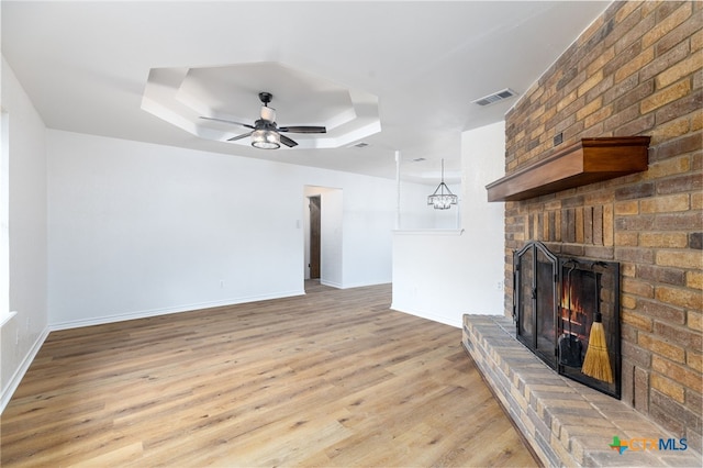 unfurnished living room with a raised ceiling, light hardwood / wood-style flooring, a brick fireplace, and ceiling fan