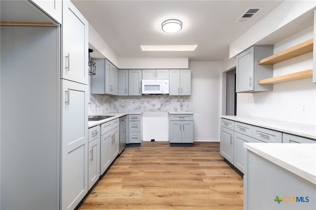 kitchen with tasteful backsplash, gray cabinetry, stainless steel dishwasher, and light wood-type flooring