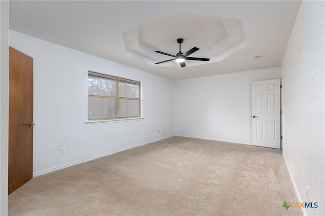 spare room featuring a raised ceiling, ceiling fan, and light colored carpet