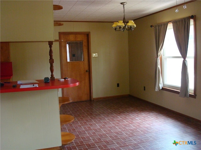 spare room with a wealth of natural light, wood walls, a chandelier, and crown molding